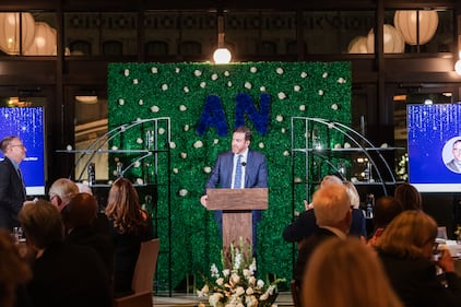 A man in a suit makes introductory remarks at an awards event.