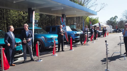 Automotive leaders stand in front of their EVs after Ionna's ribbon cutting.