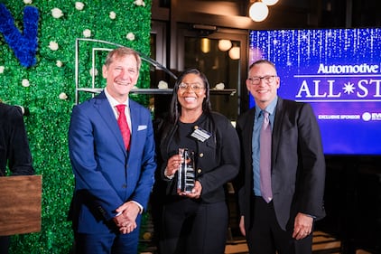 A woman holds an awards trophy next to two event co-hosts.