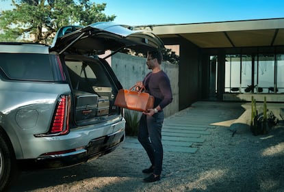 A man loading a suitcase into the back of the 2026 Cadillac Escalade IQL electric full-size SUV.