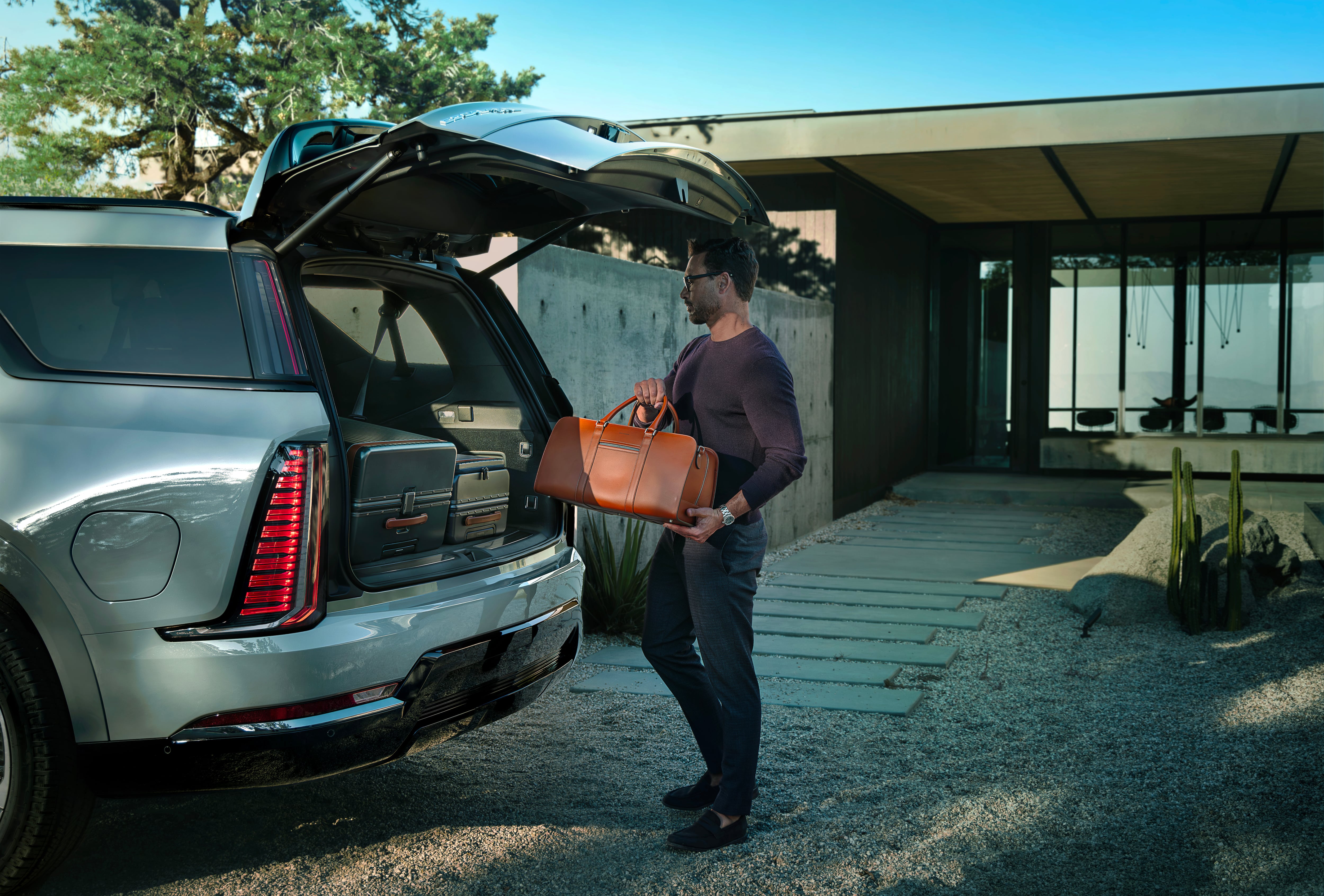 A man loading a suitcase into the back of the 2026 Cadillac Escalade IQL electric full-size SUV.