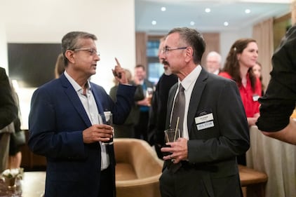 Two men with drinks talk to each other during a cocktail hour at an awards ceremony.