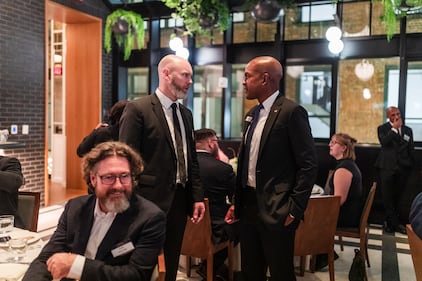 Two men standing talk during a dinner party at a gala event.