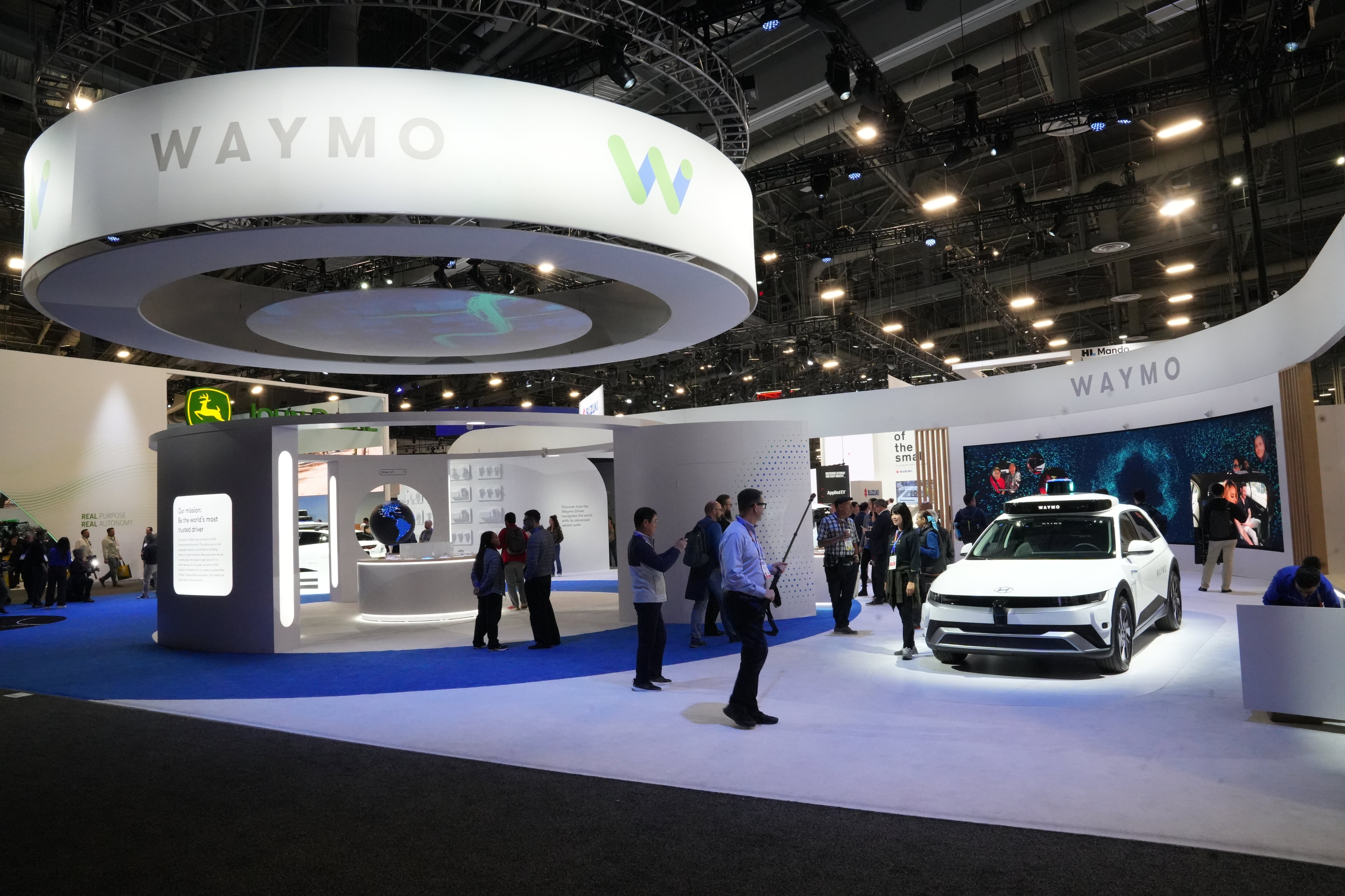 A white car surrounded by onlookers at a technology show display.