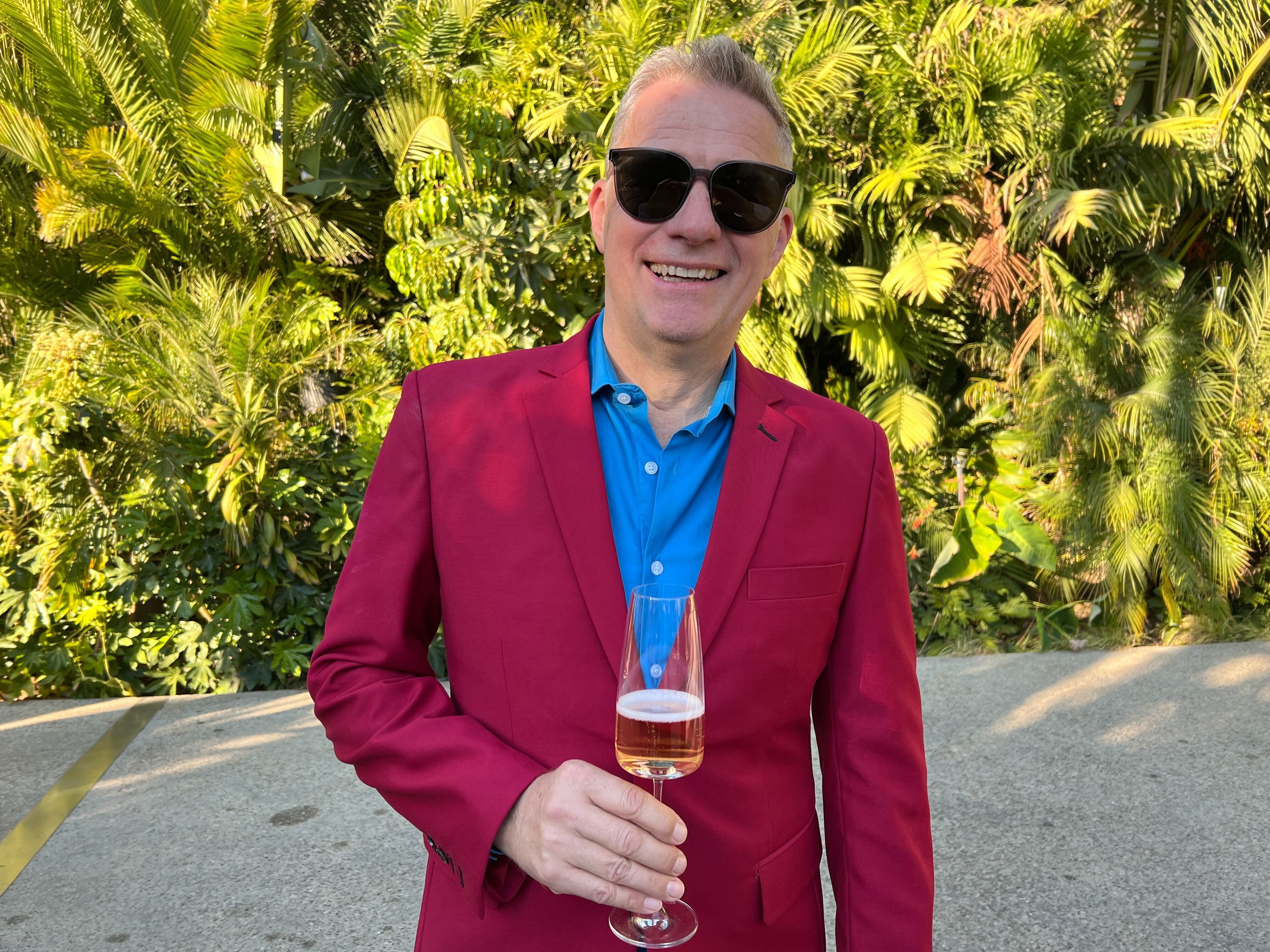 Man in a crimson suit and sunglasses holds a glass of champagne