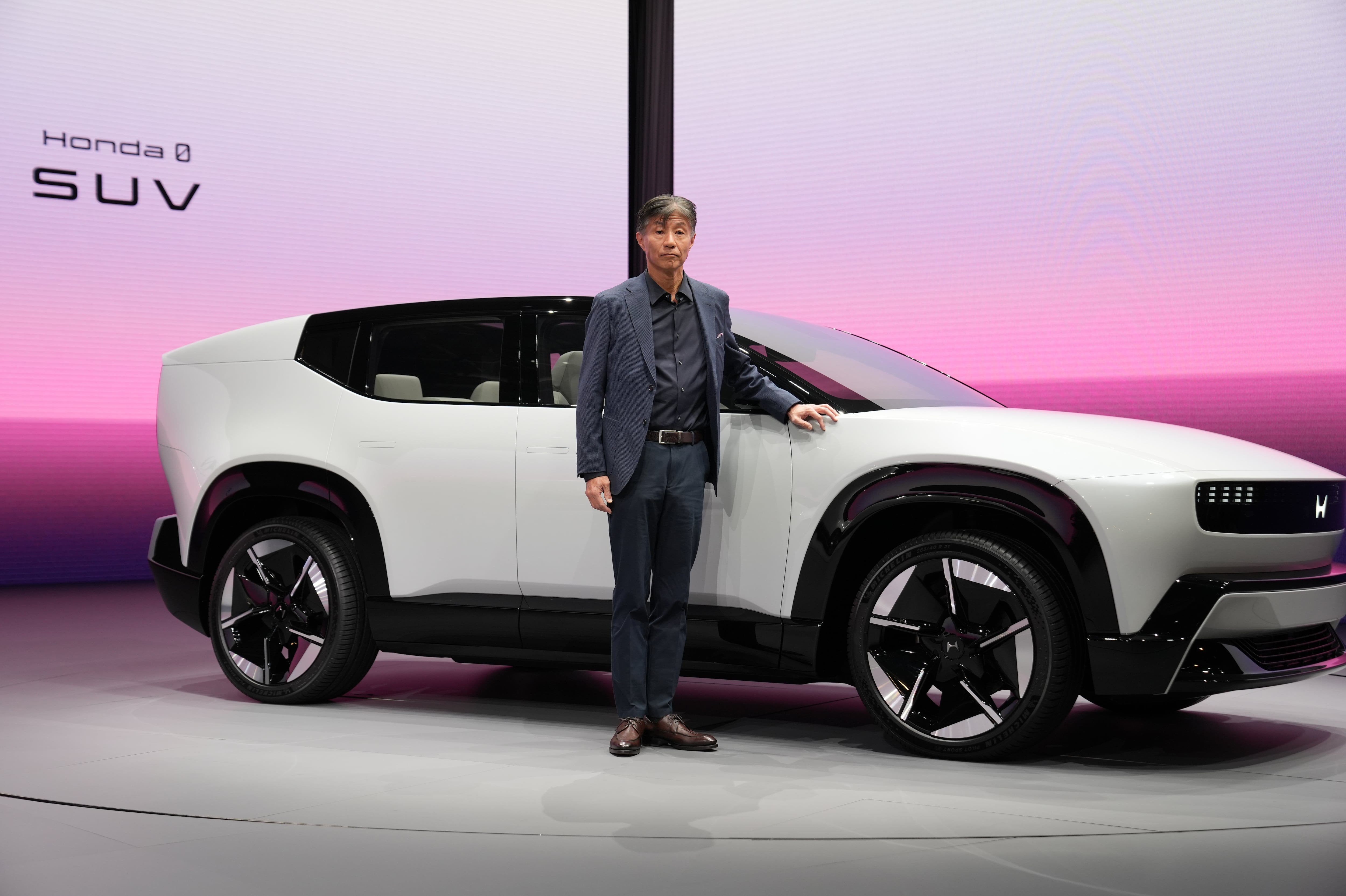 A man in a dark blazer by a white electric SUV prototype.